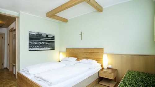 Herzlich willkommen in unserem Hotel in Matrei am Brenner Hellgrünes Gästezimmer mit Holzbett, Bild und Holzkreuz an der Wand