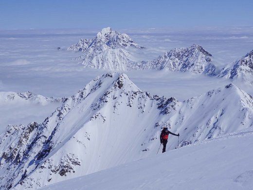 Herzlich willkommen in unserem Hotel in Matrei am Brenner Bergsteiger im roten Rucksack wandert durch verschneite Alpen mit Wolkenschicht darunter