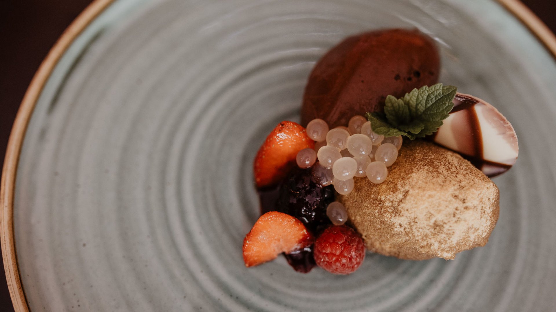 Herzlich willkommen in unserem Hotel in Matrei am Brenner Gourmetdessert mit Schokolade, Beeren und Minzblatt auf grauem Teller
