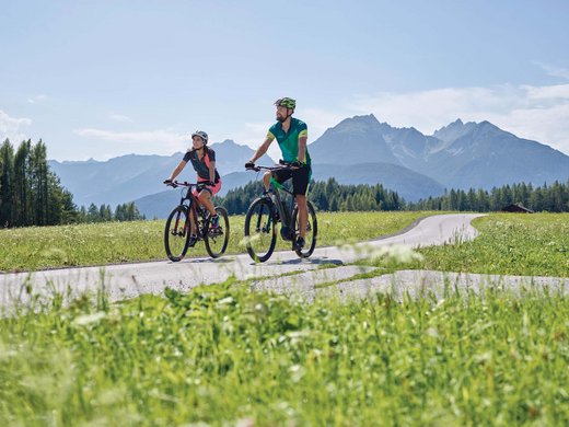 Dein Parkhotel in Matrei am Brenner Zwei Radfahrer fahren auf Landstraße mit Bergen und Wiesen im Hintergrund
