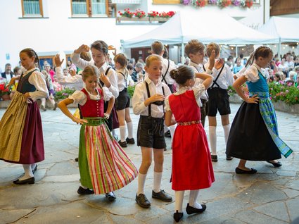 By car to Italy: stopover in Wipptal Children dancing in traditional costumes at a festival with an audience
